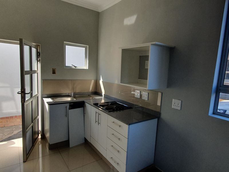 A compact kitchen featuring built-in cabinetry, stone countertops, a gas hob, and direct access to an outdoor area through a glass door.
