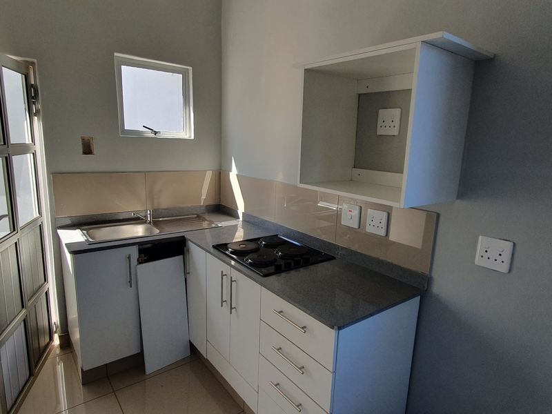 Compact kitchen featuring built-in cabinetry, stone countertops, a hob, and a stainless steel sink, with direct access to an outdoor area.