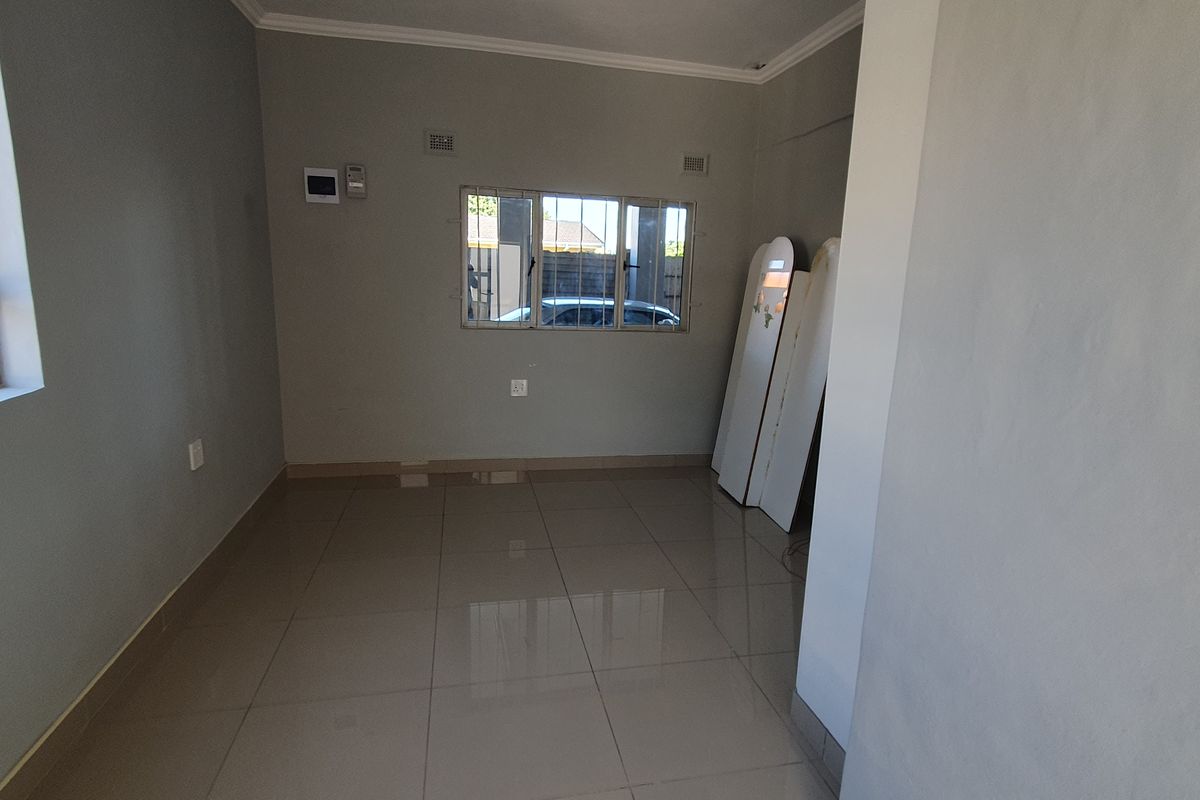 An empty, neutrally painted living area featuring large format floor tiles and aluminium-framed windows, offering a clean canvas for interior design.