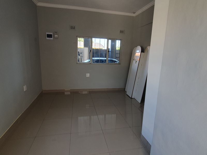 An empty, neutrally painted living area featuring large format floor tiles and aluminium-framed windows, offering a clean canvas for interior design.