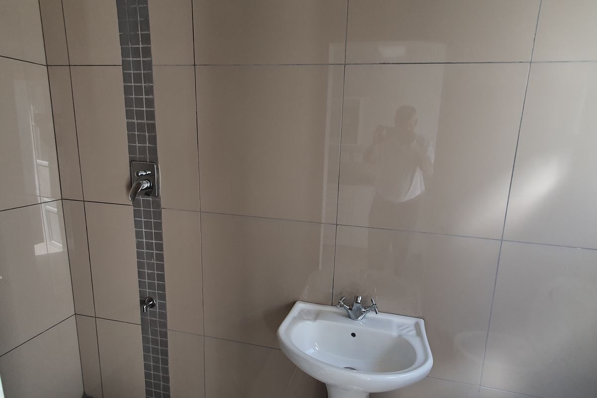 A functional bathroom space featuring neutral wall tiling with a decorative mosaic accent strip, a pedestal basin, and integrated shower plumbing.