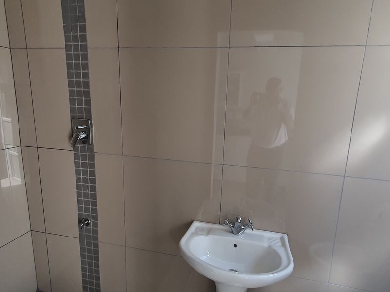 A functional bathroom space featuring neutral wall tiling with a decorative mosaic accent strip, a pedestal basin, and integrated shower plumbing.