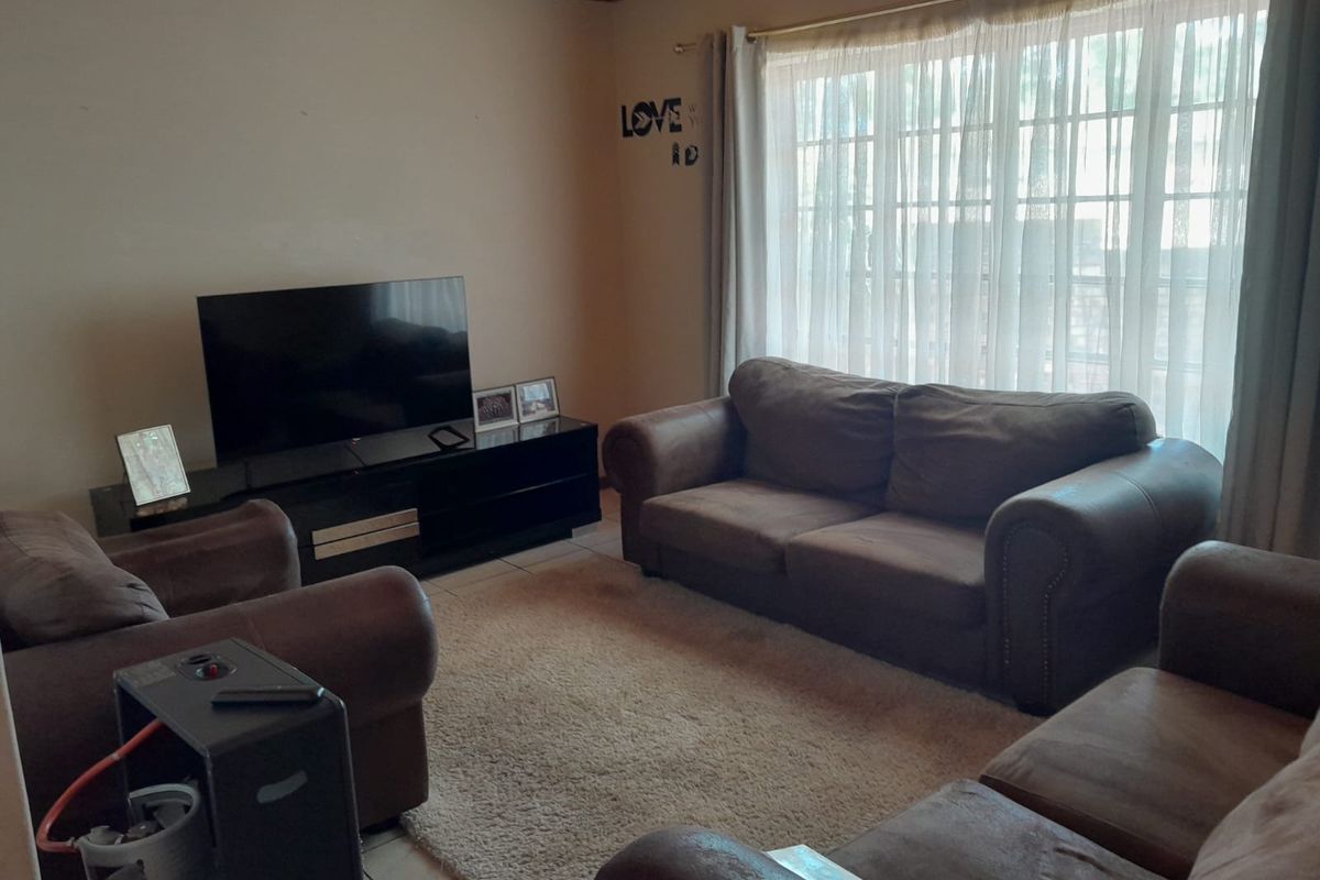 A comfortable living room featuring tiled flooring, a warm wooden ceiling, and a large window that allows for natural light.