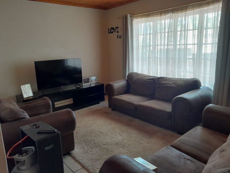 A comfortable living room featuring tiled flooring, a warm wooden ceiling, and a large window that allows for natural light.