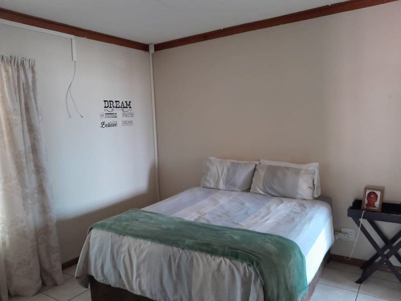A simple bedroom featuring tiled flooring and timber ceiling trim, currently furnished with a double bed.
