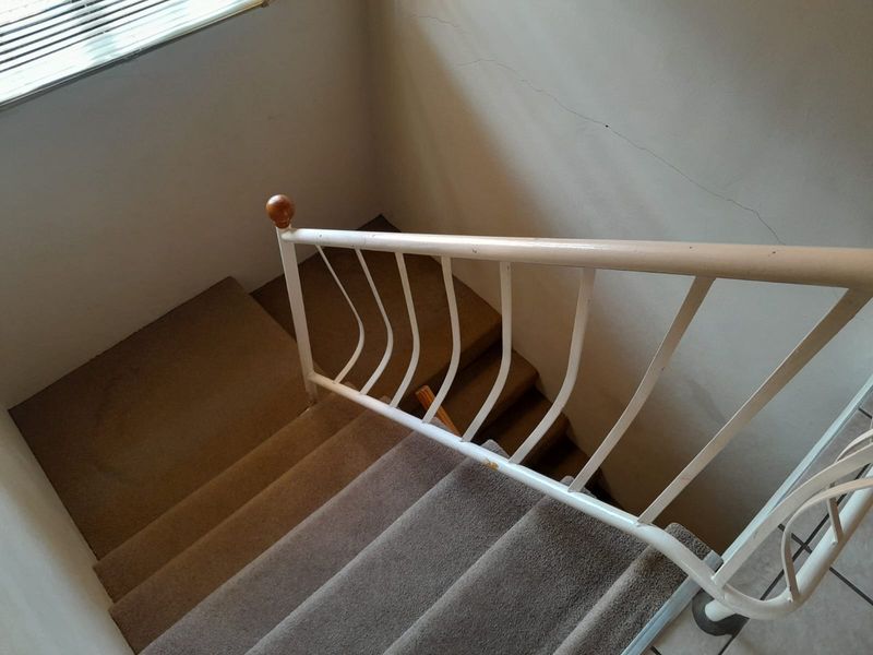 A carpeted staircase featuring a white metal balustrade, showing signs of wear including cracked wall plaster and chipped paint on the railing.