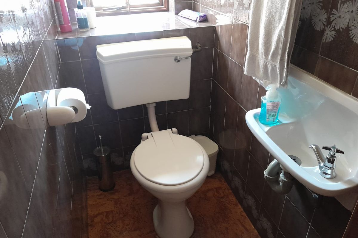 A compact guest bathroom featuring a standard toilet, wall-mounted basin, and full-height decorative wall tiling.