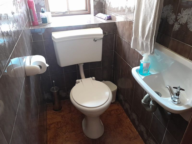 A compact guest bathroom featuring a standard toilet, wall-mounted basin, and full-height decorative wall tiling.