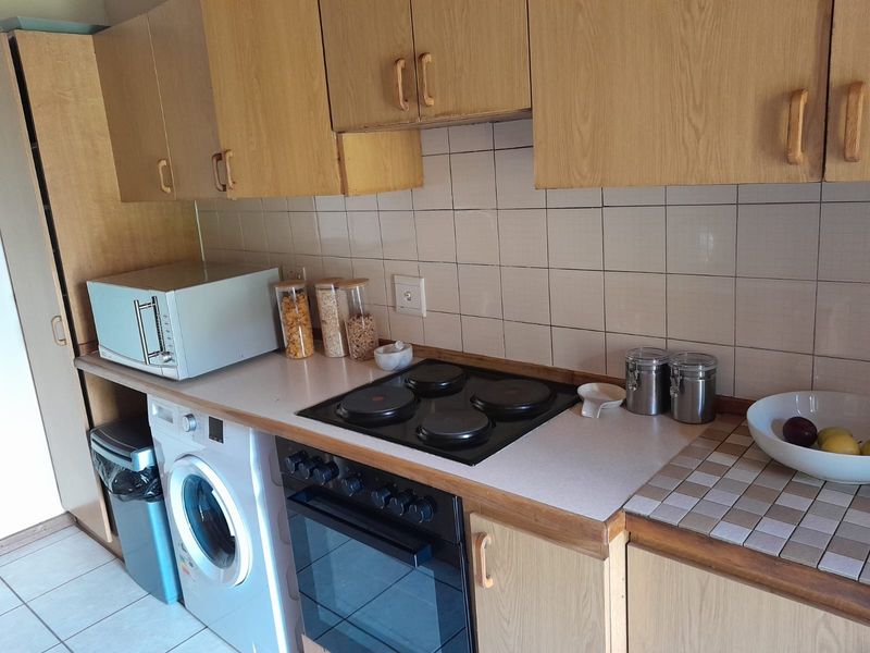 A functional kitchen featuring laminate cabinetry, a tiled backsplash, an electric hob, and a built-in oven with integrated laundry appliance space.