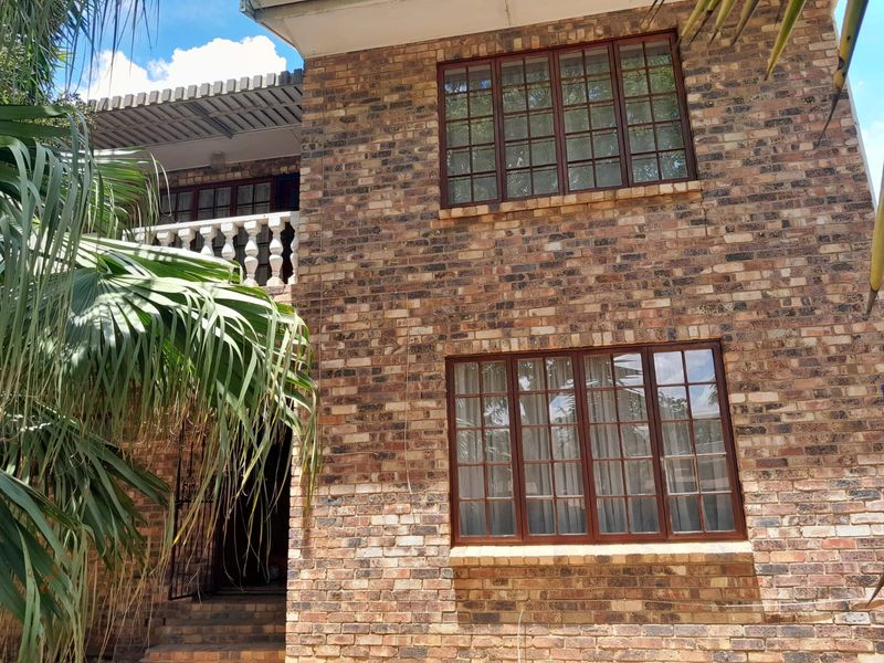 Front elevation of a double-storey townhouse featuring face brick construction, timber-framed windows, and an upper-level balcony with a decorative balustrade.