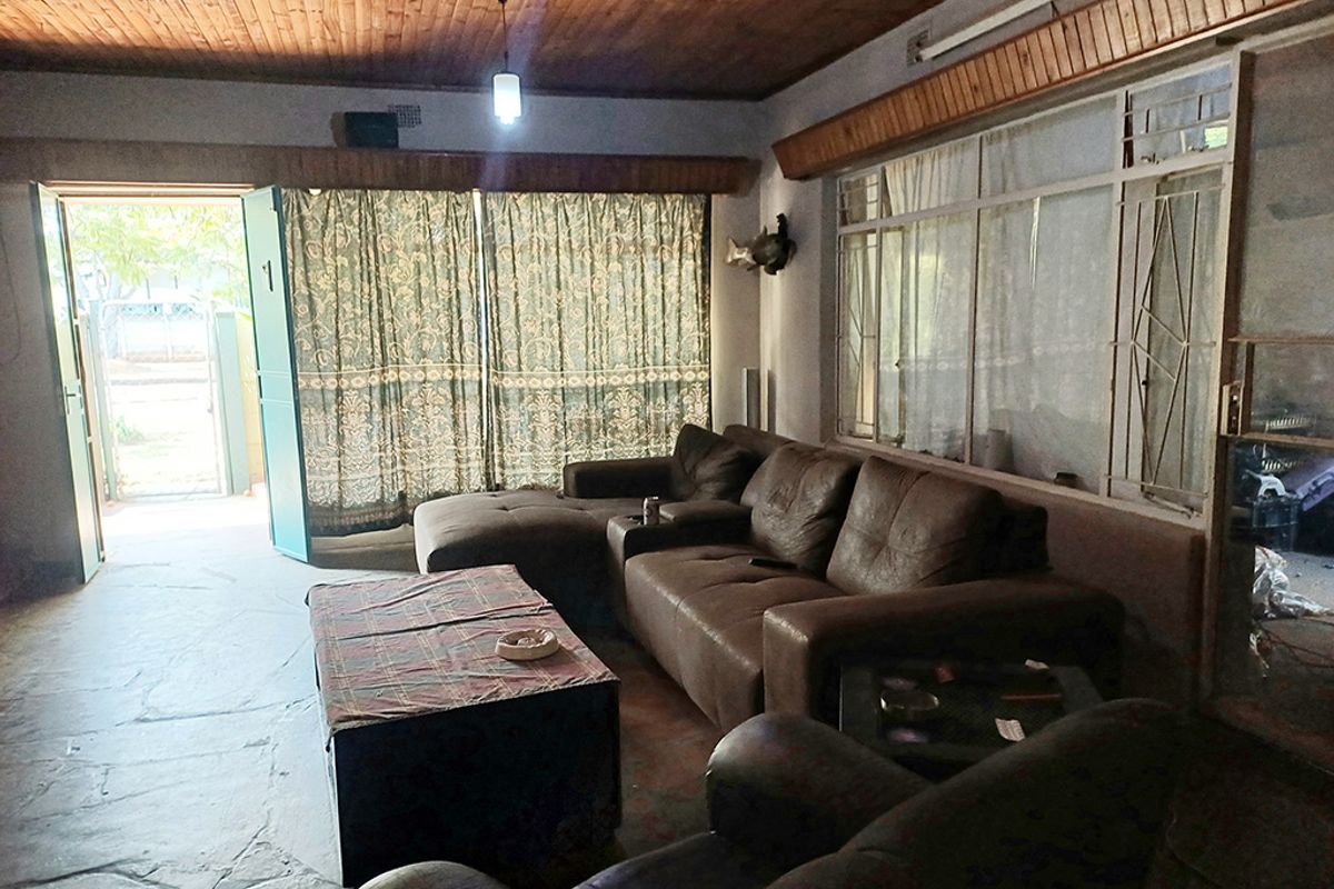 Spacious living room featuring a timber tongue and groove ceiling, stone flooring, and large windows with security bars, offering direct access to the exterior.