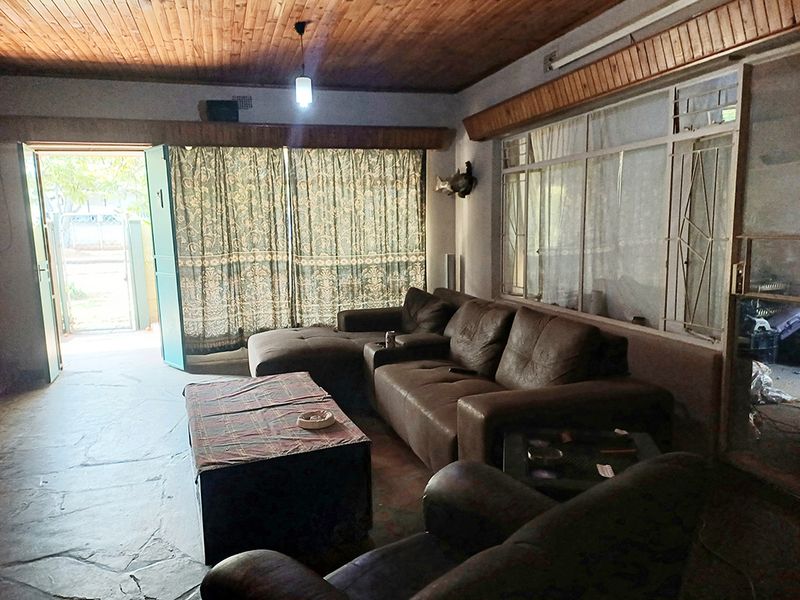 Spacious living room featuring a timber tongue and groove ceiling, stone flooring, and large windows with security bars, offering direct access to the exterior.