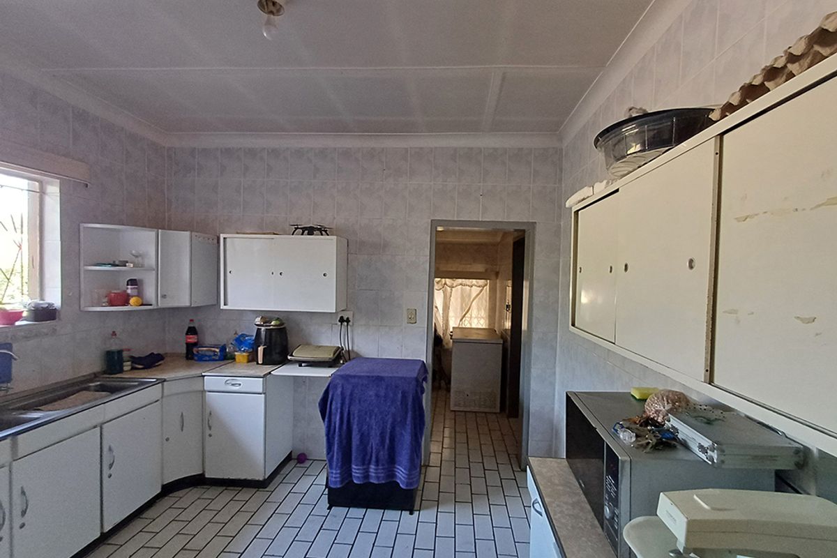 A dated kitchen featuring tiled walls and flooring, built-in cabinetry, and a stainless steel sink, offering potential for a modern renovation.