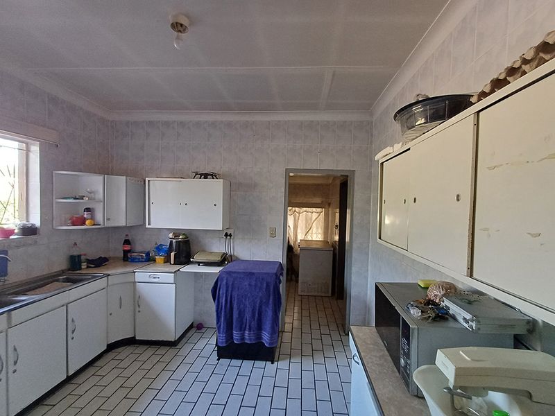 A dated kitchen featuring tiled walls and flooring, built-in cabinetry, and a stainless steel sink, offering potential for a modern renovation.