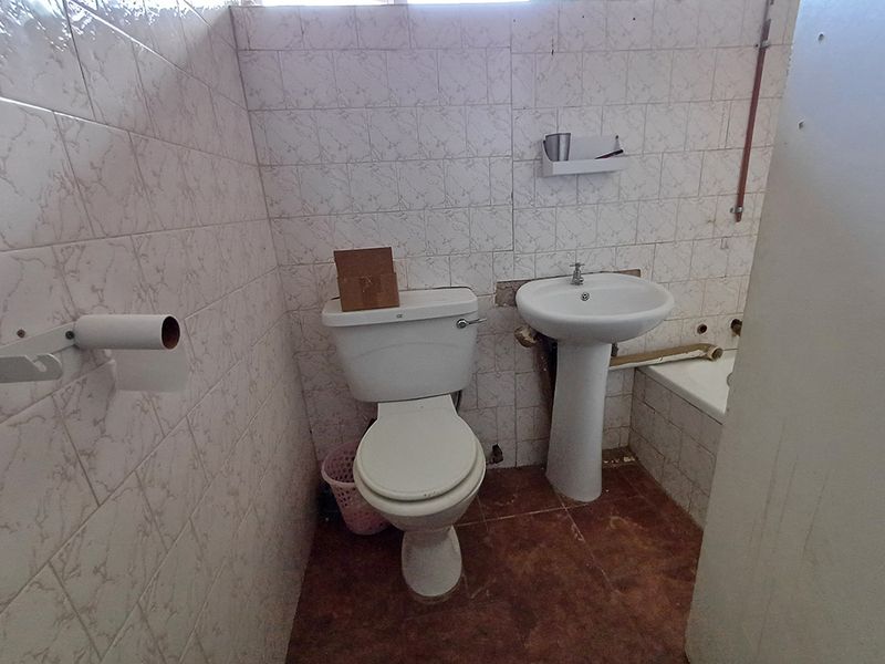 A dated bathroom featuring a pedestal basin, toilet, and bathtub with tiled finishes, currently requiring renovation and repair to exposed plumbing and wall surfaces.