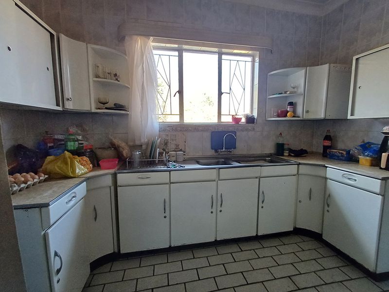 A dated kitchen featuring white built-in cabinetry, tiled backsplash, and tiled flooring, offering a functional layout with potential for modern renovation.