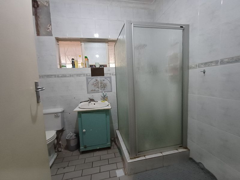 A functional bathroom featuring a shower enclosure, vanity basin, and toilet, with tiled finishes throughout. The space requires cosmetic updates and repairs.