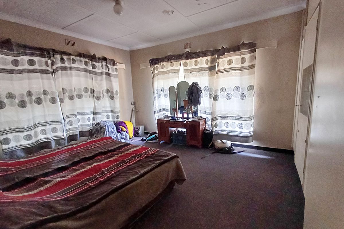 Spacious bedroom featuring built-in cupboards, carpeted flooring, and ceiling tiles requiring maintenance and cosmetic updates.