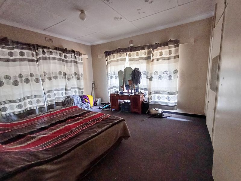 Spacious bedroom featuring built-in cupboards, carpeted flooring, and ceiling tiles requiring maintenance and cosmetic updates.