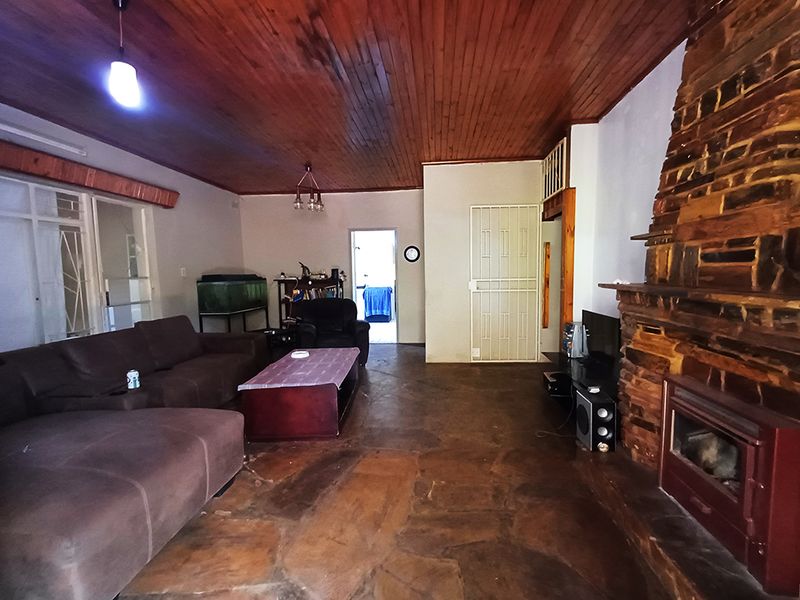 Spacious living room featuring a prominent stone fireplace with a built-in wood-burning stove, timber-clad ceiling, and rustic flagstone flooring.