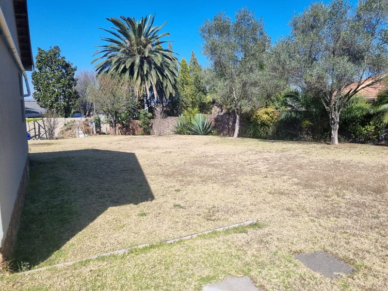 A spacious backyard featuring a large lawn area, mature trees, and a brick boundary wall.