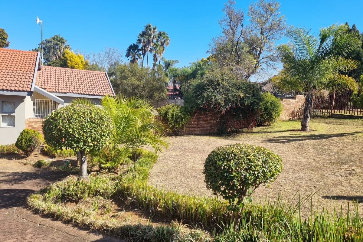 A spacious rear garden featuring a well-maintained lawn, established trees, landscaped shrubbery, and a paved area adjacent to the house.