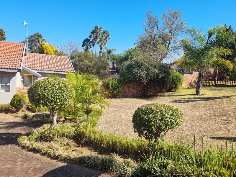 A spacious rear garden featuring a well-maintained lawn, established trees, landscaped shrubbery, and a paved area adjacent to the house.