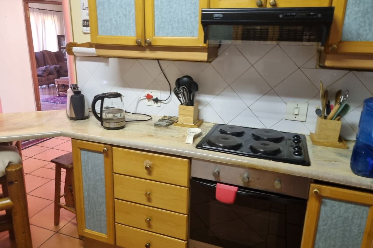 A functional kitchen featuring wooden cabinetry, laminate countertops, a built-in oven with hob, and an extractor fan, finished with a tiled backsplash.