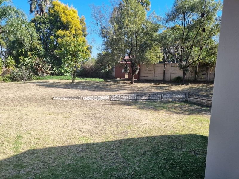 A spacious backyard garden featuring a tiered lawn with a low stone retaining wall, mature trees, and a perimeter boundary wall.