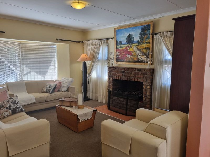 A cozy living room featuring a traditional brick fireplace, a large bay window, and neutral wall finishes.