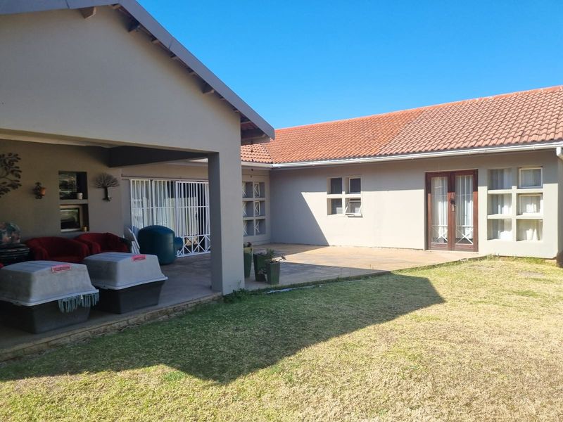 Rear view of the property featuring a covered patio area, paved courtyard, and a spacious lawn with access via french doors.