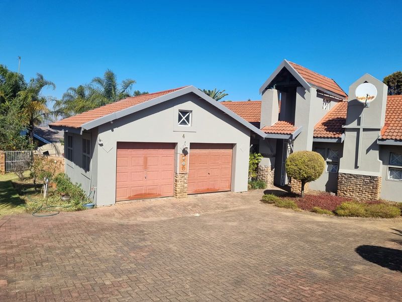 Front elevation of a residential property featuring a double garage, paved driveway, and distinctive architectural roof lines with stone cladding accents.