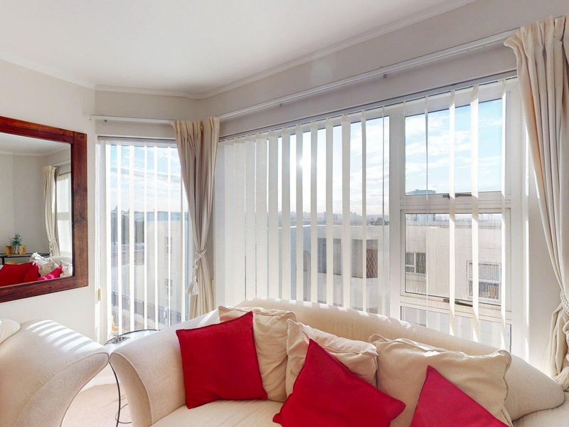 A bright living room area featuring a large bay window with vertical blinds and curtain tracks, offering natural light and an urban view.