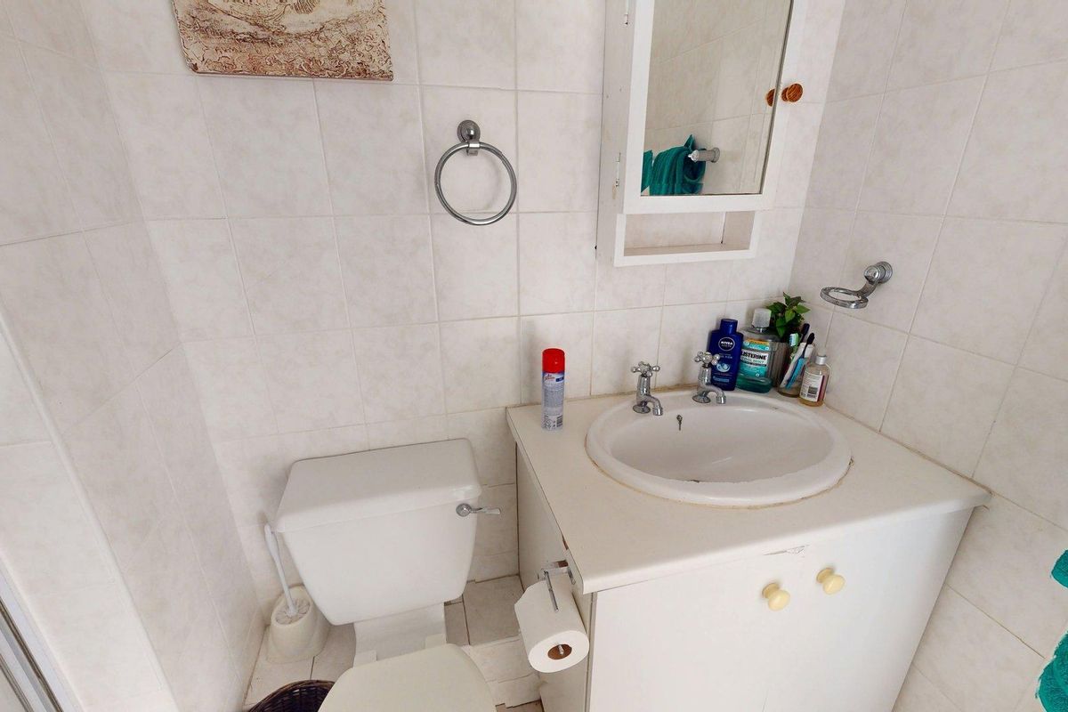 Compact bathroom featuring a vanity cabinet with integrated basin, toilet, and wall-mounted storage cabinet, finished with neutral ceramic wall tiling.
