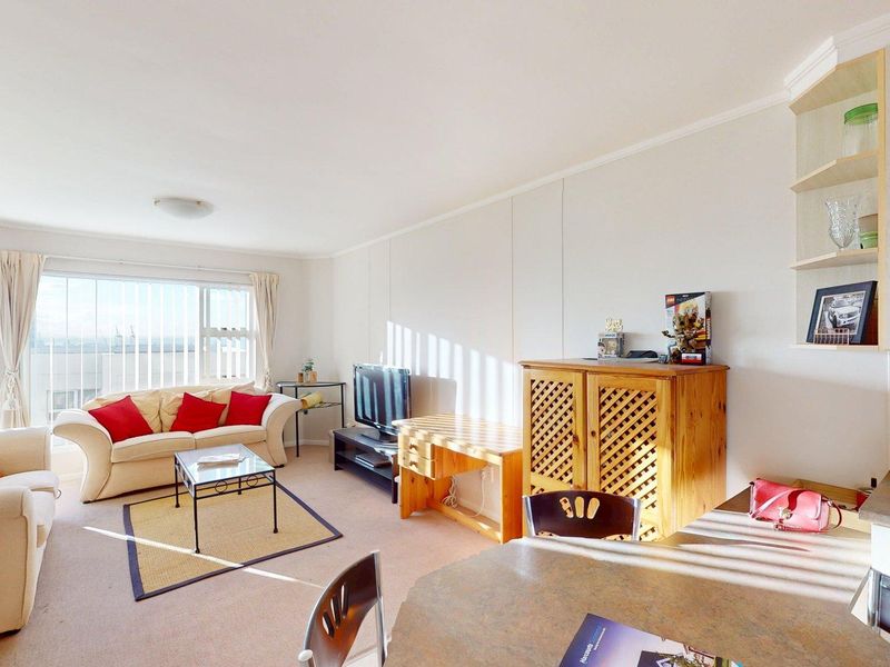 Open-plan living and dining area featuring neutral carpeting, built-in shelving, and large sliding glass doors providing natural light and access to the balcony.