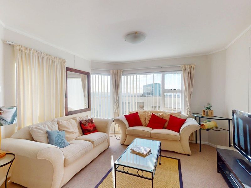 A bright living room featuring carpeted flooring, large windows with vertical blinds, and a neutral color palette, offering a comfortable and functional space.