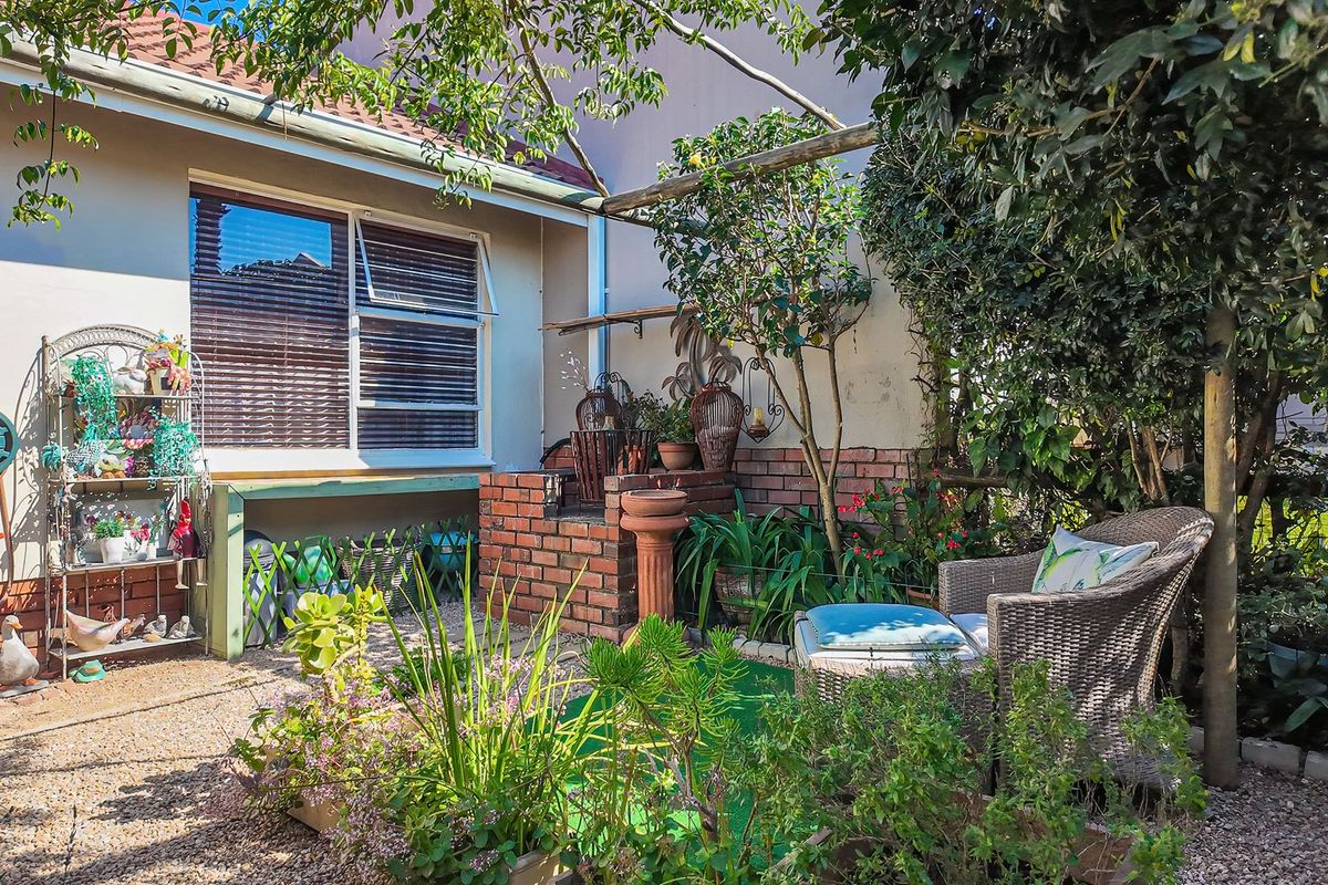 A private rear courtyard featuring a brick built-in braai, gravel ground cover, and a timber pergola structure set against the townhouse exterior.