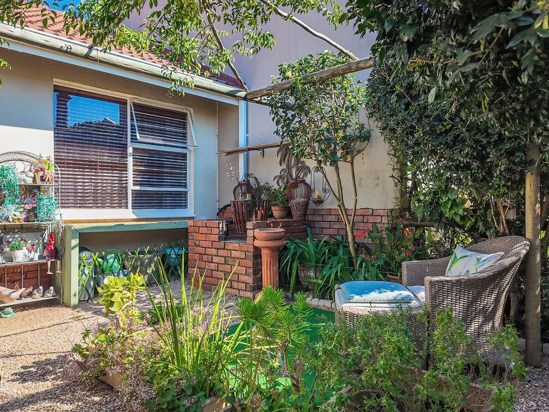 A private rear courtyard featuring a brick built-in braai, gravel ground cover, and a timber pergola structure set against the townhouse exterior.