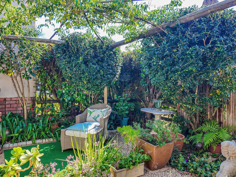 A private, landscaped garden area featuring a timber pergola, established greenery, and a brick retaining wall, creating a tranquil outdoor retreat.