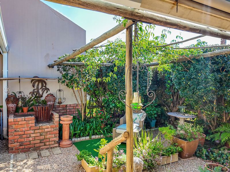A rustic outdoor patio area featuring a timber pergola and a built-in brick braai, set within a landscaped garden space.