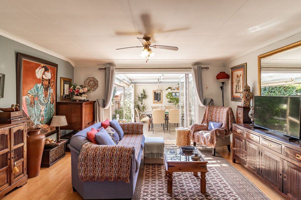 A well-maintained living room featuring laminate flooring, a ceiling fan, and large folding glass doors that open onto an adjacent patio area.
