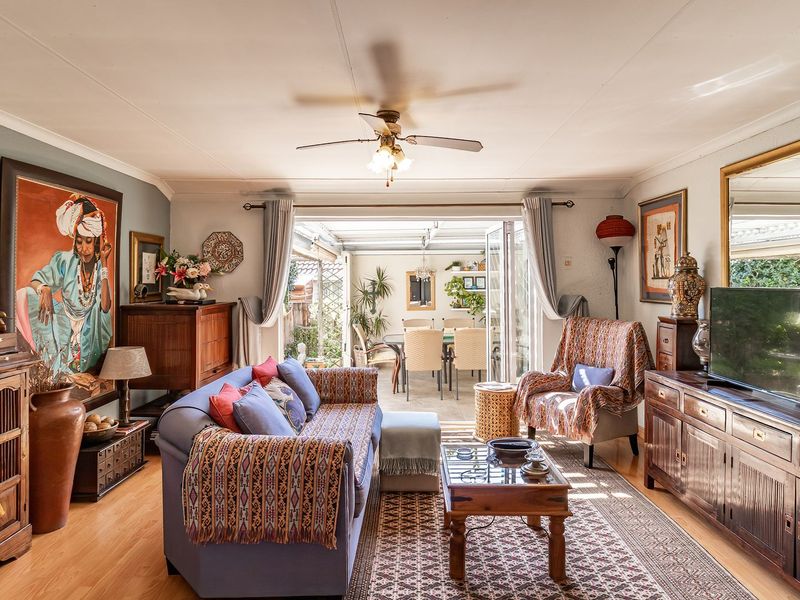 A well-maintained living room featuring laminate flooring, a ceiling fan, and large folding glass doors that open onto an adjacent patio area.