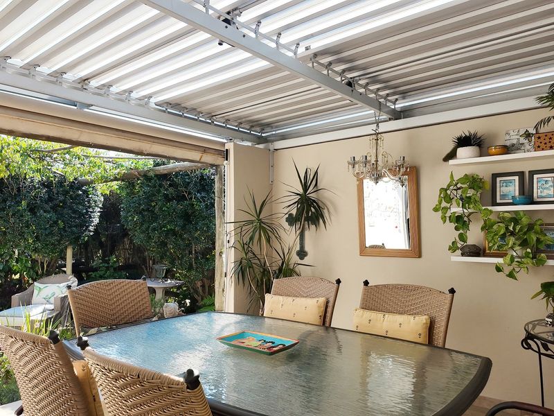 A covered outdoor patio area featuring a corrugated metal roof, providing a sheltered space for dining and relaxation overlooking the garden.
