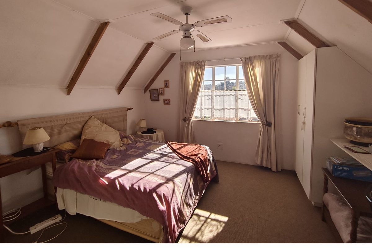 A cozy bedroom featuring exposed timber ceiling beams, a ceiling fan, built-in wardrobe storage, and natural light through a window.