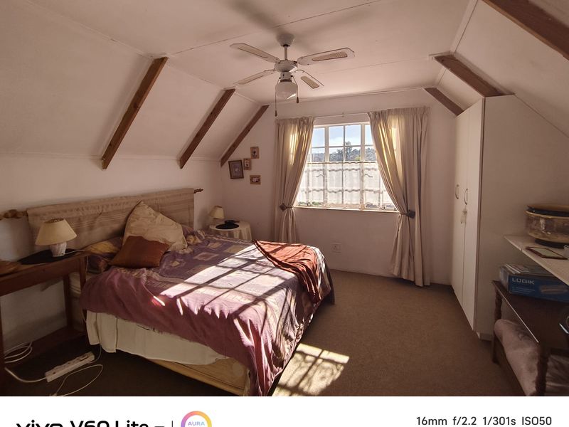 A cozy bedroom featuring exposed timber ceiling beams, a ceiling fan, built-in wardrobe storage, and natural light through a window.