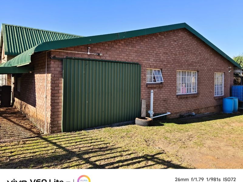 Rear view of a brick house featuring a large sliding metal door, green corrugated roof, and steel-framed windows.