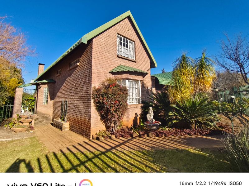 Front view of a brick house featuring a metal roof and paved walkway, surrounded by established garden landscaping.