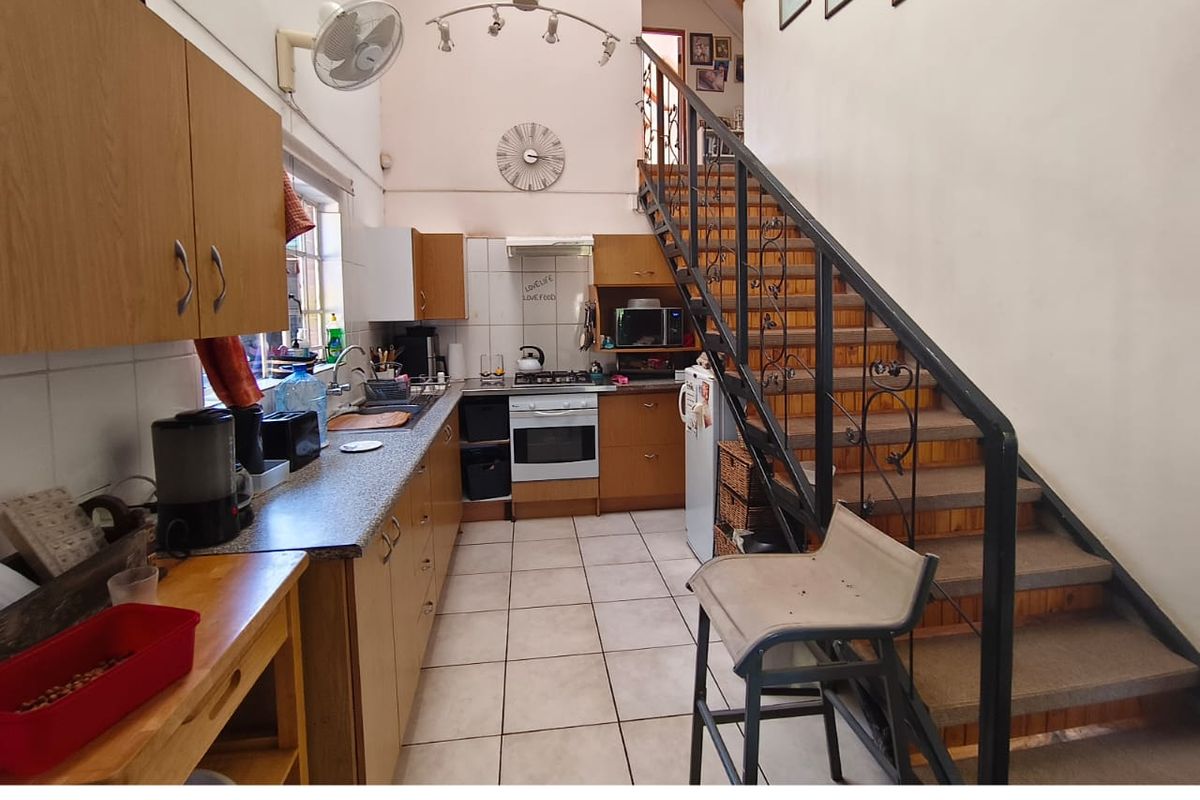 A functional kitchen featuring built-in cabinetry, gas hob, and oven, with an integrated staircase leading to an upper level under a vaulted ceiling.