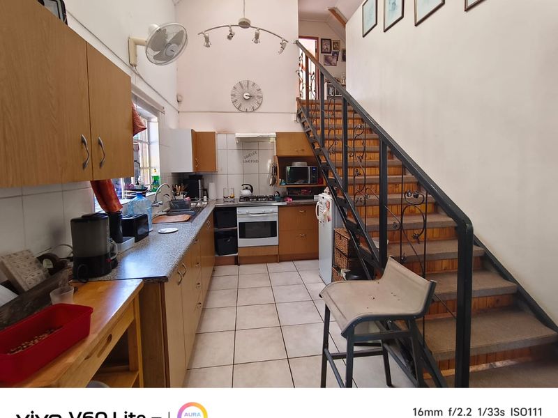 A functional kitchen featuring built-in cabinetry, gas hob, and oven, with an integrated staircase leading to an upper level under a vaulted ceiling.