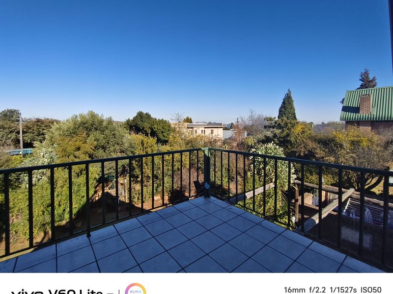An elevated balcony featuring tiled flooring and a metal safety railing, offering an open view of the surrounding garden and neighborhood.